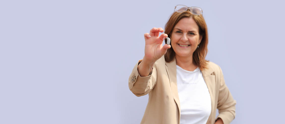 Carola Ise die ein Hörgerät in die Kamera hält