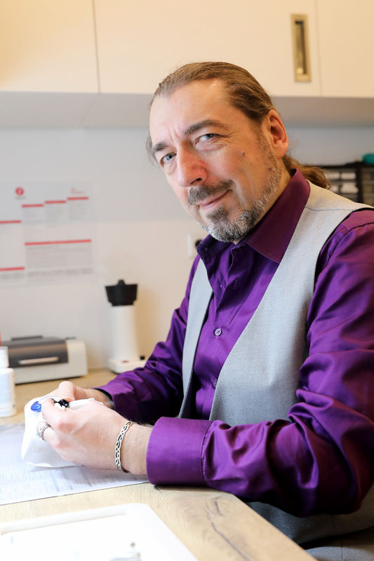 Ein Herr sitzt am Schreibtisch und lächelt in die Kamera. 